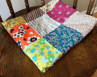 May include: A patchwork quilt made of various colorful fabrics with floral and geometric patterns. The quilt is folded and placed on a wooden chair.