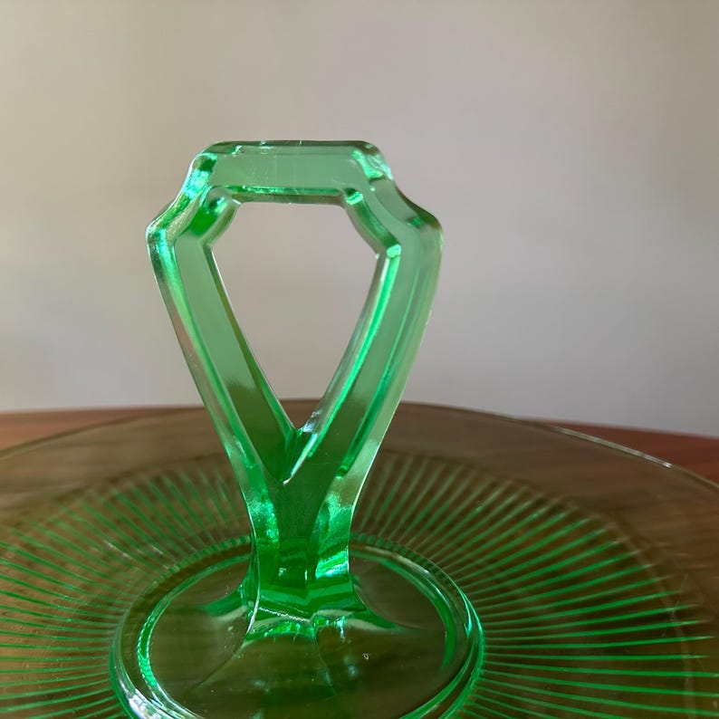 Może przedstawiać: Zbliżenie zielonej szklanej tacy do serwowania z uchwytem. Uchwyt ma kształt rombu, a taca ma żebrowany wz&oacute;r. Szkło jest jasne, p&oacute;łprzezroczyste zielone.