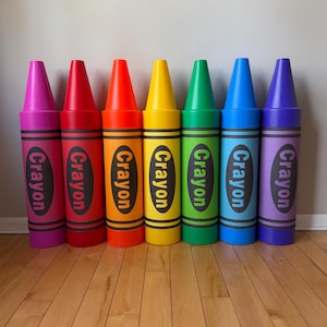 May include: Seven large, colorful crayon-shaped decorations. Each crayon is a different color, including pink, red, orange, yellow, green, blue, and purple. The word "Crayon" is printed vertically on each crayon.