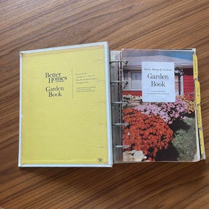 May include: A yellow Better Homes and Gardens Garden Book with a revised edition copyright 1961, 1971, 1981. The book is open to a page with a photo of a red brick house with a flower garden in front. The text on the page reads "Better Homes & Gardens Garden Book A year-round guide to practical home gardening."