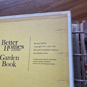May include: A yellow book cover with the title "Better Homes and Gardens Garden Book" in black text. The book is a revised edition with copyright dates 1951, 1954, and 1961. The publisher is Meredith Publishing Company, located in Des Moines, Iowa.