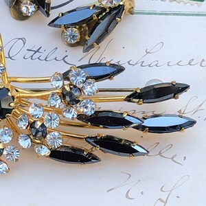 Puede incluir: Un broche de tono dorado con diamantes de imitaci&oacute;n negros y transparentes. El broche tiene forma de abanico con m&uacute;ltiples puntas. Los diamantes de imitaci&oacute;n est&aacute;n engastados en un metal de tono dorado.