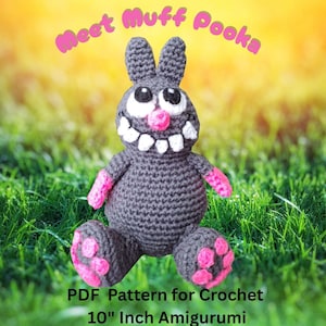 Puede incluir: Un amigurumi de conejo gris tejido a ganchillo con detalles rosas, incluyendo patas y brazos. El conejo tiene una amplia sonrisa y ojos grandes. El texto "Meet Muff Pooka" y "PDF Pattern for Crochet 25.4 cm Amigurumi" son visibles.