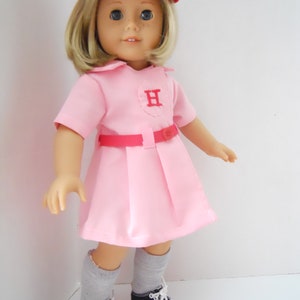 May include: A pink and red doll wearing a baseball uniform with a red cap that says "H" on the front. The doll is wearing grey socks and black and white sneakers.