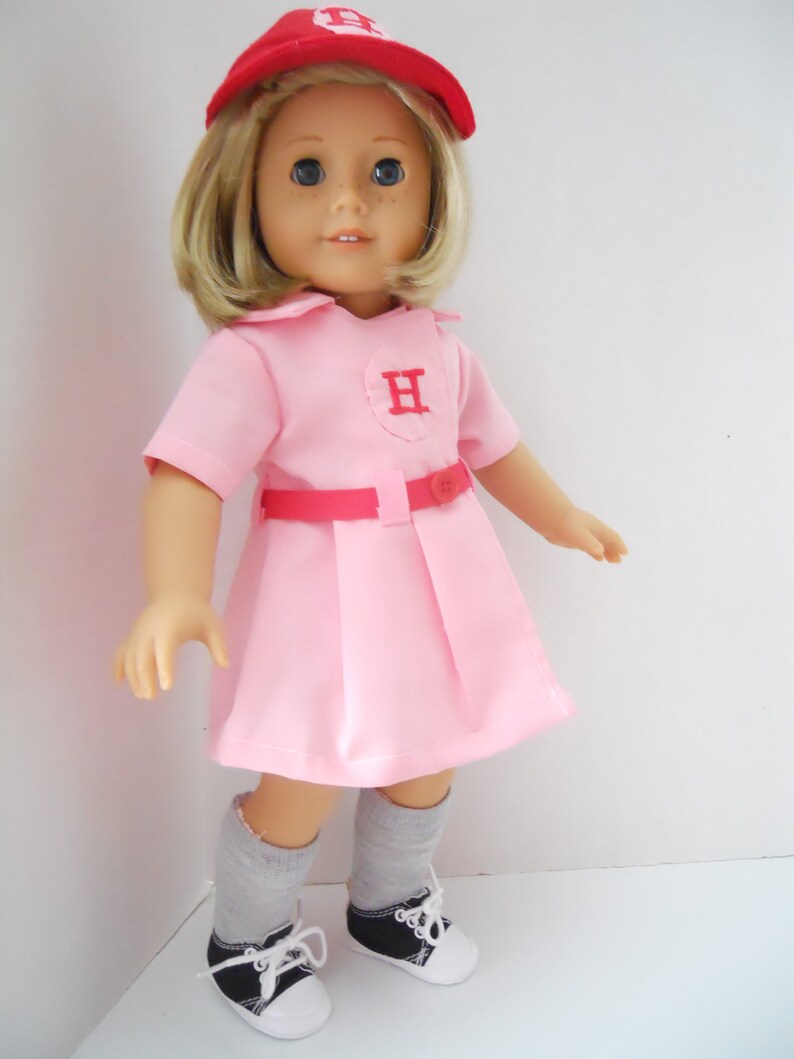 May include: A pink and red doll wearing a baseball uniform with a red cap that says "H" on the front. The doll is wearing grey socks and black and white sneakers.
