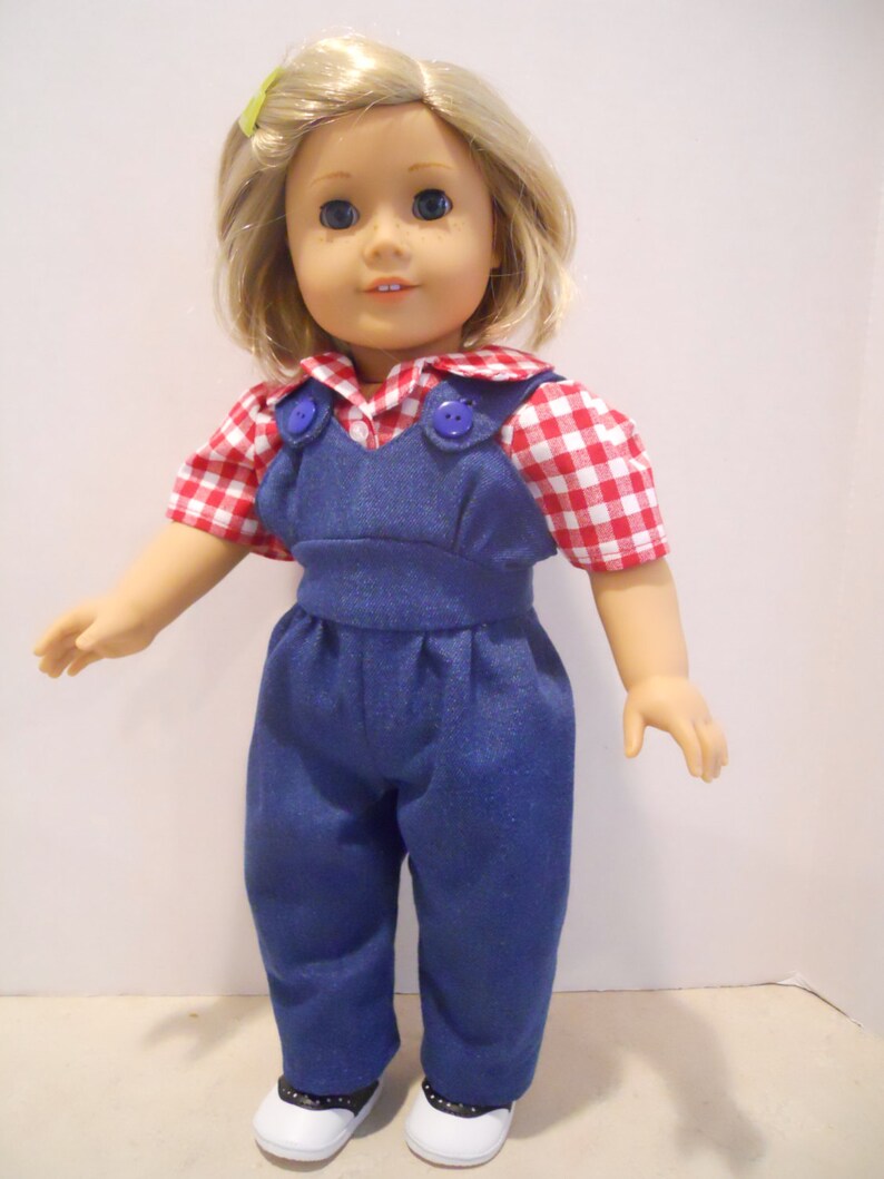 Puede incluir: Una mu&ntilde;eca con una camisa de cuadros rojos y blancos con un mono vaquero azul y zapatos blancos.