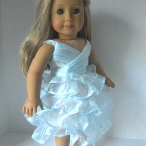 May include: A doll wearing a light blue dress with a ruffled skirt and white shoes.