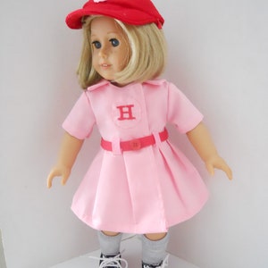May include: A pink dress with a red belt and a red baseball cap with a white "H" on it. The doll is wearing grey socks and black and white sneakers.