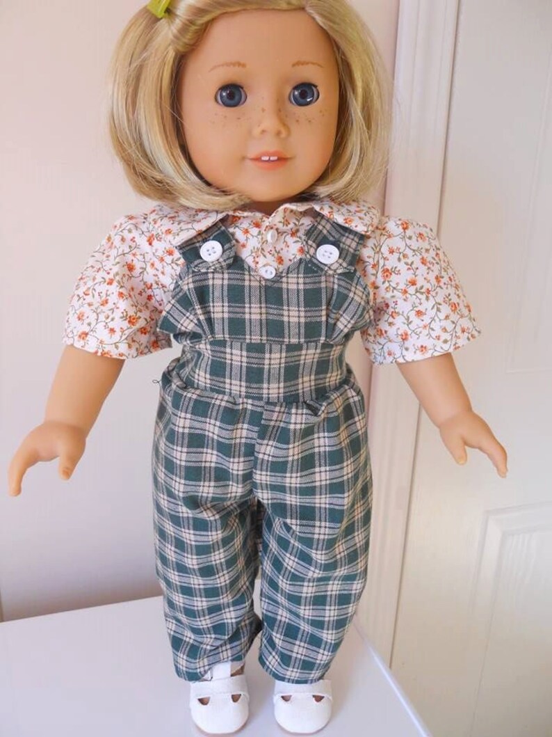 Puede incluir: Una mu&ntilde;eca con un vestido de peto de cuadros verdes y blancos con una camisa de estampado floral. La mu&ntilde;eca tiene el pelo rubio y los ojos azules.