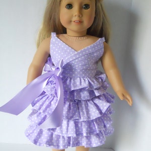 May include: A purple and white polka dot dress with a ruffled skirt and a matching purple ribbon. The dress is designed for a doll.