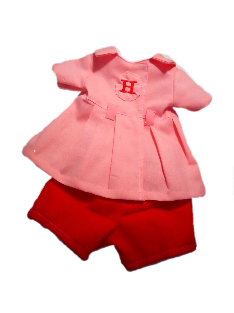 May include: A pink dress with a white circle and the letter "H" embroidered on the back, paired with red shorts.