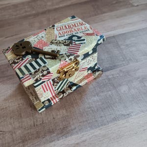 May include: A small wooden box with a keyhole and a gold latch. The box is covered in colorful patterned paper with the text "You should know that you're charming and ever so sweet" on the front.