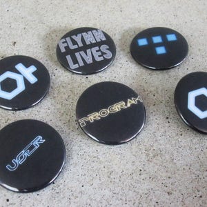 May include: Six black and white round buttons with different text and graphics. The buttons feature the text "Flynn Lives", "Program", "User", and the graphics of a grid, a hexagon, and a circle with a line through it.