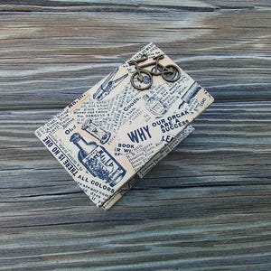 May include: A vintage-style box with a newspaper print design featuring a bottle of liquid, an hourglass, and the text "Why Our Organs Are A Success". A small metal bicycle charm is attached to the box.