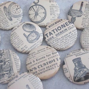 May include: A collection of vintage-style button pins featuring various designs, including a compass, a bottle of ink, and a stationery store advertisement. The buttons are printed on a cream-colored background with black text and illustrations.