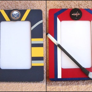 May include: Two wooden picture frames decorated with hockey team colors and logos. The frame on the left is blue, yellow, and gray with a Buffalo Sabres logo. The frame on the right is red, white, and blue with a Detroit Red Wings logo.
