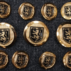 May include: Ten gold-colored buttons with a black and gold lion crest design. The buttons have a raised, textured surface and a plaid pattern.