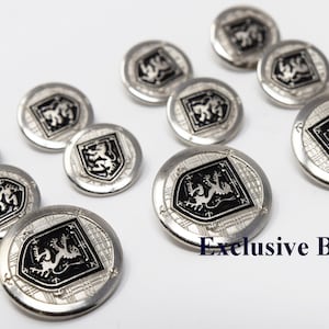 Puede incluir: Diez botones plateados con un diseño en blanco y negro que presenta un león rampante. Los botones tienen un borde elevado y texturizado y un centro liso. El texto "Exclusive Buttons" es visible en la esquina inferior derecha de la imagen.