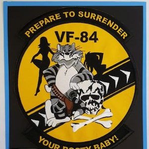 May include: A yellow and black embroidered patch with the text "Prepare to Surrender", "VF-84", and "Your Booty Baby!"  The patch features a cartoon cat holding a skull and crossbones.