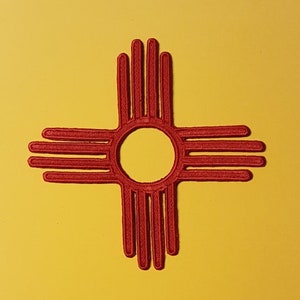 May include: Red embroidered patch of the Zia symbol, a traditional symbol of the Zia Pueblo people of New Mexico. The symbol is a stylised sun with four rays, each with eight points.