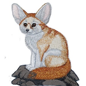 May include: A white and orange embroidered patch of a fennec fox sitting on a rock. The fox has large ears and a bushy tail.