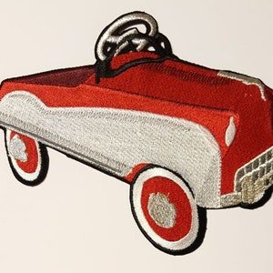 May include: Red and white embroidered iron-on patch of a toy car. The car has a white body and red wheels.