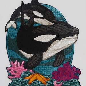 Puede incluir: Parche bordado con dos orcas blancas y negras nadando en agua turquesa con coral y estrellas de mar.