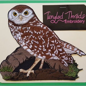 May include: Embroidered patch of a brown and white owl perched on a rock with green foliage. The patch is from Tangled Threads Embroidery.