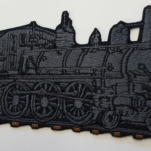 Puede incluir: Un parche bordado en blanco y negro de un tren de locomotora de vapor vintage con un vagón de carbón. El tren está en una vía con traviesas marrones.