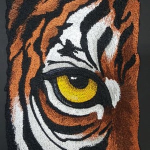 May include: Close-up of a tiger's eye with orange and black stripes. The eye is yellow with a black pupil.
