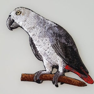 May include: Embroidered iron-on patch of a gray parrot perched on a branch. The parrot has a red tail and a black eye.