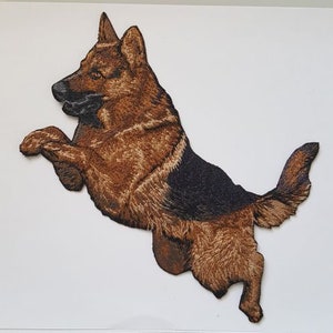 May include: Embroidered patch of a brown and black German Shepherd dog jumping in the air.