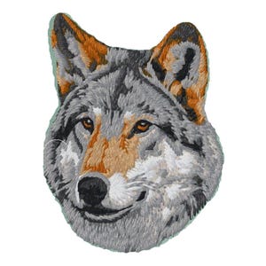 May include: An embroidered patch featuring the detailed head of a wolf. The design uses shades of grey, white, black, and tan thread to depict the animal's fur, pointed ears, and focused amber eyes, with a solid black nose and mouth area.