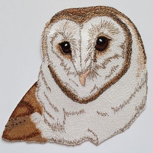 May include: Embroidered patch featuring a detailed barn owl. The owl has brown eyes, a light brown beak, and a white and brown feathered design. The patch is likely for clothing or accessories.