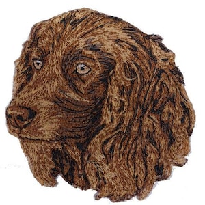 May include: Embroidered patch of a brown and black dog with a long, flowing coat. The dog's head is turned to the side, and its eyes are visible. The patch is made of a soft, textured fabric.