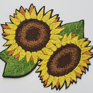 以下が含まれることがあります： 緑の葉が付いた刺繍されたひまわりパッチが2つ。ひまわりは黄色で、中心は茶色です。