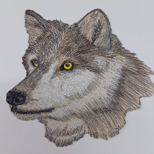 May include: Embroidered patch of a wolf's head with a detailed design. The wolf has a light brown and gray fur with yellow eyes.