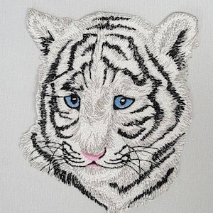 May include: Embroidered white tiger face patch with blue eyes. The patch is detailed with black stitching and a pink nose.