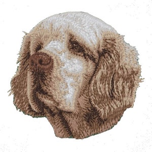 May include: Embroidered patch of a brown and white dog with floppy ears. The dog's face is visible and has a brown nose and brown eyes.