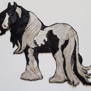 Könnte beinhalten: Schwarzer und weißer gestickter Aufnäher eines Pferdes mit langer, fließender Mähne und Schweif.