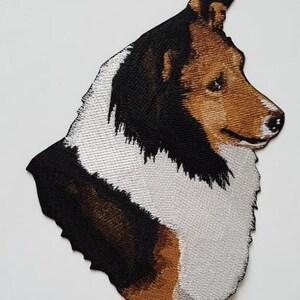 May include: Embroidered patch of a brown and white Collie dog with black fur around its face and ears.