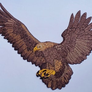 Könnte beinhalten: Gestickter brauner Adler-Patch mit gelben Krallen, die Flügel im Flug ausgebreitet.