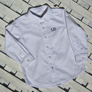 May include: White long-sleeve button-down shirt with a navy blue embroidered monogram "SJD" on the chest.