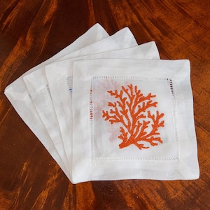 May include: Set of four white linen napkins with orange embroidered coral designs.