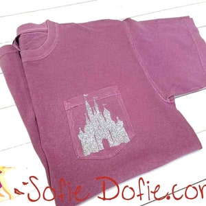 Könnte beinhalten: Ein mauvefarbenes T-Shirt mit einem silbernen Glitzer-Schloss-Design auf der Tasche.