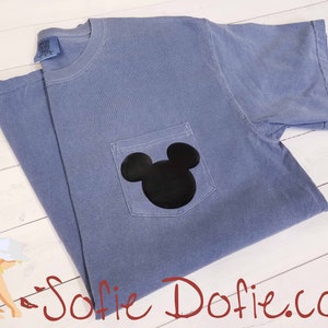 K&ouml;nnte beinhalten: Ein hellblaues T-Shirt mit einer schwarzen Mickey-Maus-Silhouette auf der Tasche.