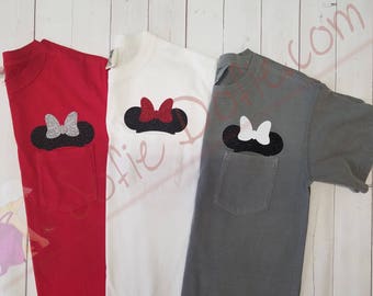 May include: Three t-shirts with a pocket on the left side. Each pocket has a different colored Minnie Mouse head with a bow. The t-shirts are red, white, and gray.