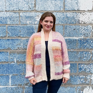 May include: A pink, yellow and purple knit cardigan with a cream-coloured knit lining. The cardigan has a relaxed fit and a long, open front.