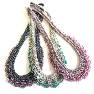 May include: Three beaded necklaces in different colors. The necklaces are made of small, metallic beads and have a scalloped edge. The colors are black, silver, and pink.