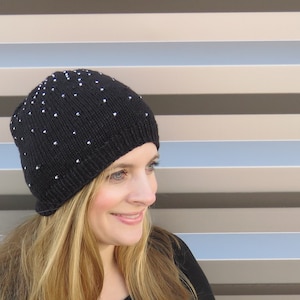 May include: A black knit beanie with silver embellishments. The beanie is worn by a person with long blonde hair.